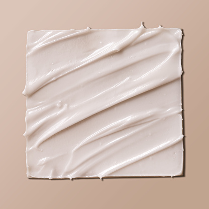 Cosmetic smear of white creamy texture on a beige background. Face cream or body lotion swipe swatch.