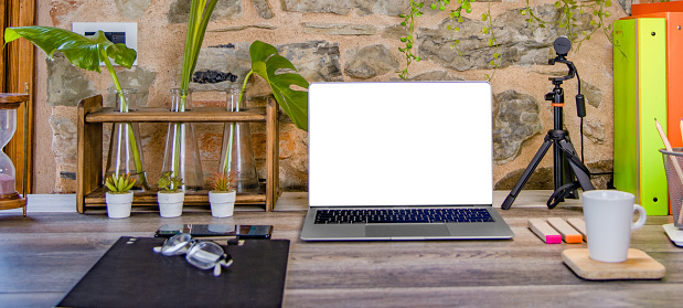 Notebook with White Screen, Glasses, Hourglass, Plants, Stationary, Pencils and a Coffee Cup on the Desk
