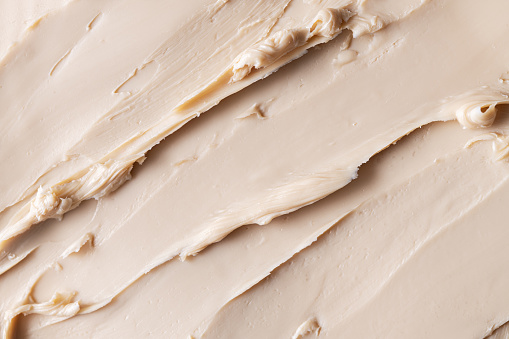 Close-up view of a textured cosmetic clay. Cosmetic product beige texture with visible strokes and ridjes, highlighting its smooth and soft.