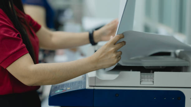 istock A woman is using a printer to print a document. She is wearing a red shirt and is holding a piece of paper in her hand 2104271688