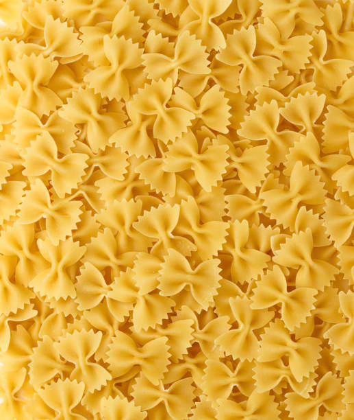 pasta italiana farfalle fundo. close-up de macarrão de gravata borboleta não cozida. conceito criativo de alimentos. vista superior, diretamente acima. - bow tie pasta italian cuisine bow heap - fotografias e filmes do acervo