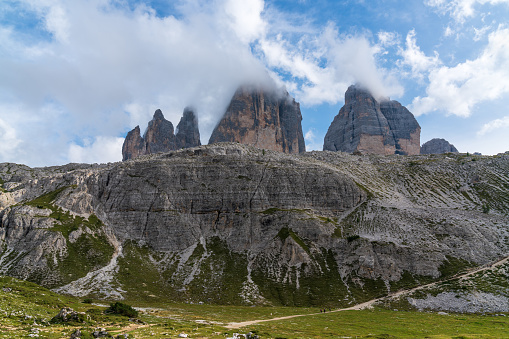 Stunning view of the mountains covered with thick clouds. Picturesque landscape with high sharp rocks, green grass, majestic trees, cloudy sky in the Dolomites, Italy. Adventure and hiking