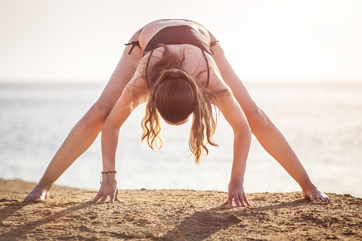 Young fitness woman doing stretching at the beach in the morning. Yoga morning routine image