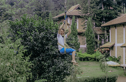 Young Indonesian male play flying fox at an outdoor tourism. Flying Fox is a game of sliding from a tree using a steel sling.