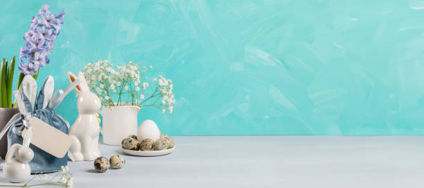 istock Easter banner. Eggs, ceramic bunnies, flowers, gift bag, blank note on turquoise. Copy space. 2104380782