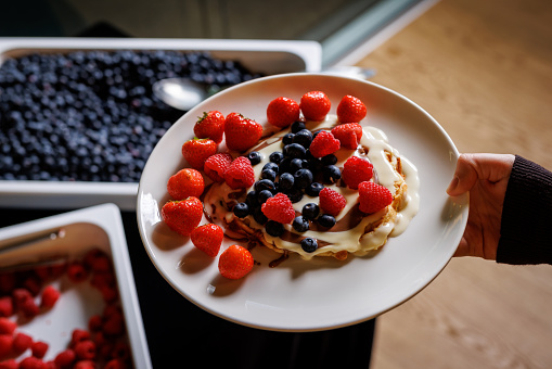 Pancakes adorned with ripe red strawberries and juicy blueberries, complemented by a luscious cream topping