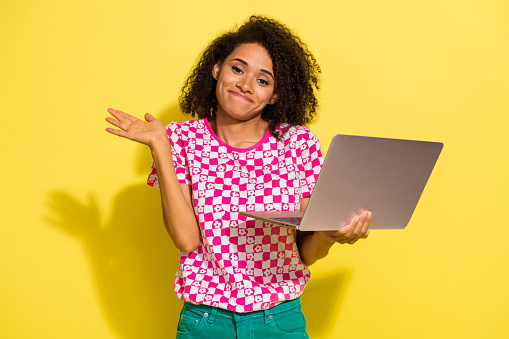 Portrait of attractive clueless person hold wireless netbook raise hand shrug shoulder isolated on yellow color background.