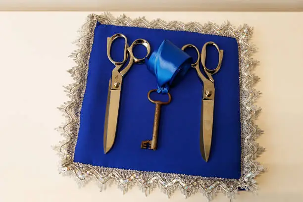 Steel scissors, adorned with a satin blue ribbon, laid on an opulent blue canvas. Ready for the grand opening