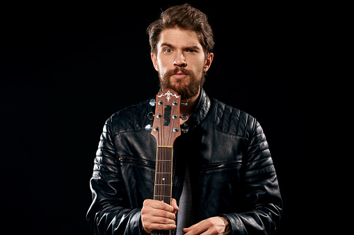 A man with a guitar in his hands leather jacket music performance rock star modern style dark background. High quality photo