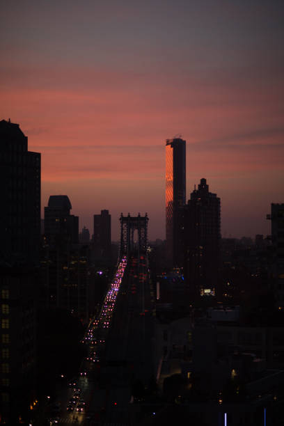This is a photograph of the Brooklyn Bridge in silhouette with a colorful sky at dusk in NYC.