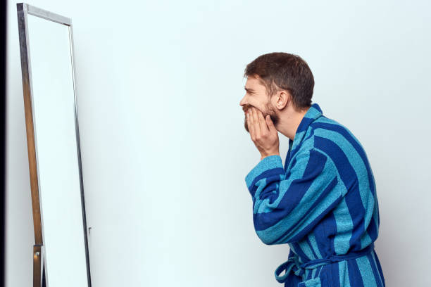 istock a man in a blue robe examines himself in a mirror in a bright room cropped view 2104536568