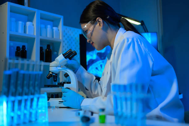 istock A woman in a lab coat is looking through a microscope 2104537741