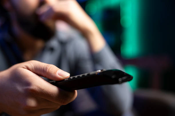 istock Close up of remote control held by man changing channels on television set 2104540734