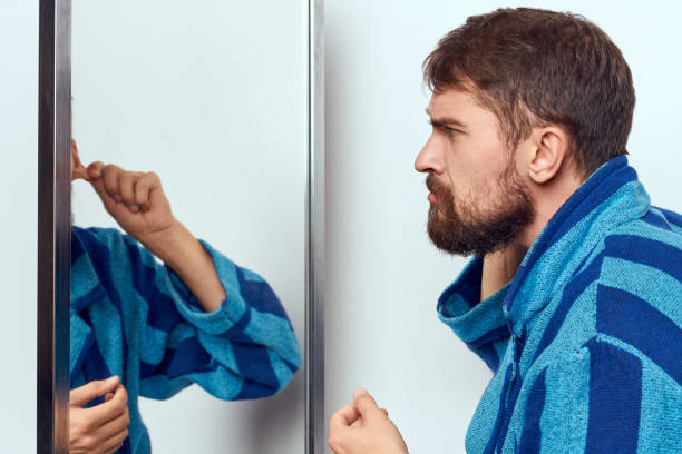 istock a man in a blue robe examines himself in a mirror in a bright room cropped view 2104543089