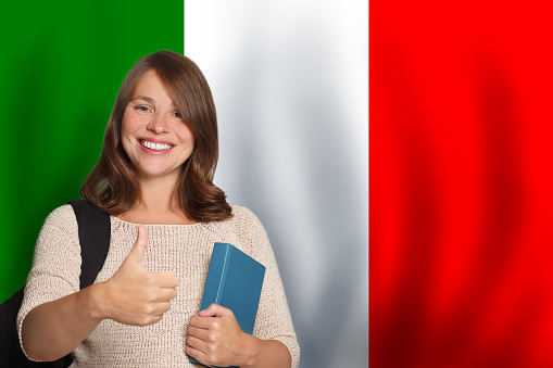 Cheerful woman student showing thumb up against Italian flag background. Travel, education and learn language in Italy concept