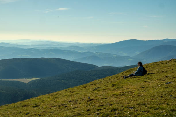 Woman sitting on grass and overlooking the European Alps from from their highest point in Austria, Schneeberg.