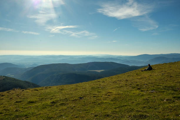 Woman sitting on grass and overlooking the European Alps from from their highest point in Austria, Schneeberg.