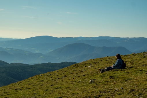 Woman sitting on grass and overlooking the European Alps from from their highest point in Austria, Schneeberg.