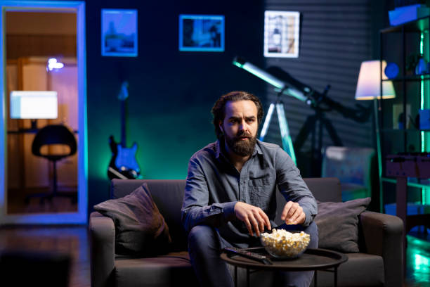 istock Lazy couch potato watching shows on TV and eating popcorn 2104564631