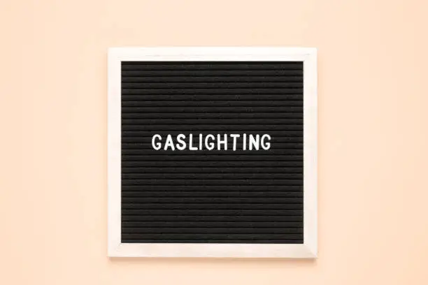 The word gaslighting on black letter board over isolated beige background. Psychological violence concept