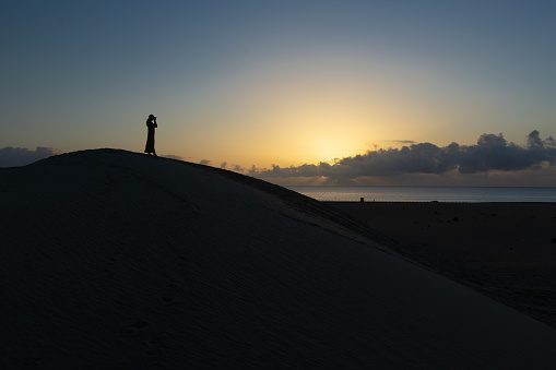 Woman on top of a dune watching the sunrise behind the clouds