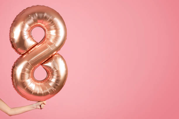 istock An anonymous person's hand holding a large, shiny rose gold number eight balloon 2104578996