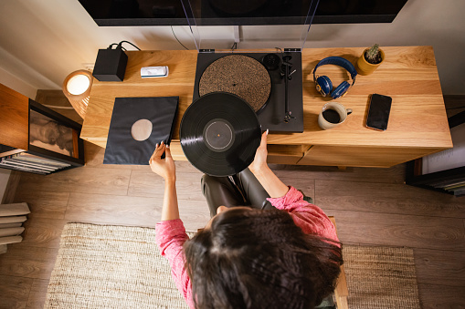 Embracing leisure time, a lady places a vinyl record on her gramophone while enjoying a cup of coffee at home.