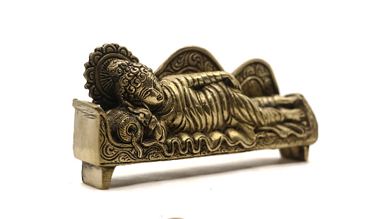 ancient figure handcrafted in gold colored metal of lord buddha sleeping on the side on a couch with pillow, with intricate details isolated
