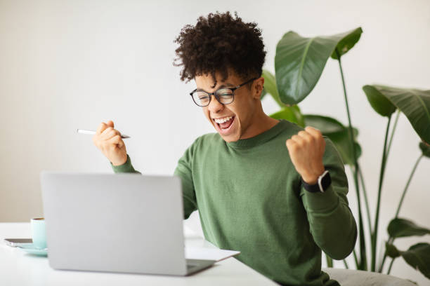 istock Emotional african american guy celebrating success, working at cafe 2104632296