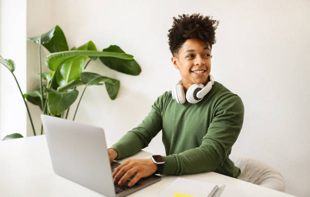 istock Happy millennial black man with wireless headphones using laptop 2104632343