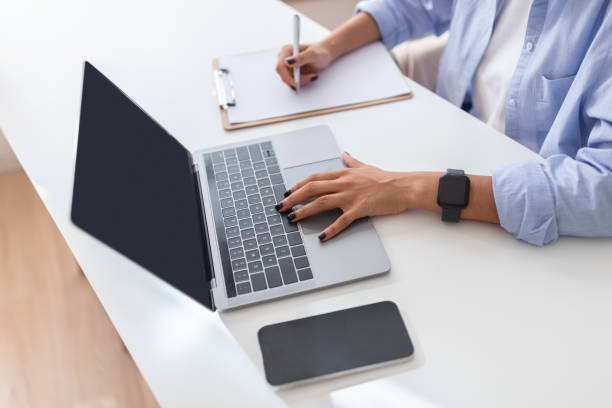 Close-up of a professional multitasking with a laptop and taking notes