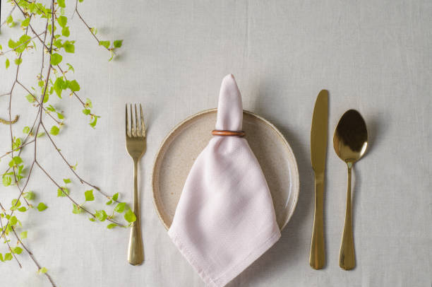 istock Table setting. Plate with pink napkin, gold cutlery lying on concrete background. Birch branch. Selective Focus 2104724337