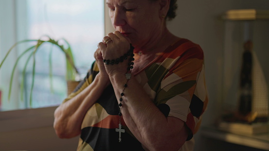 Religious Catholic older woman Praying Rosary at home in deep contemplation. Elderly person having HOPE and FAITH
