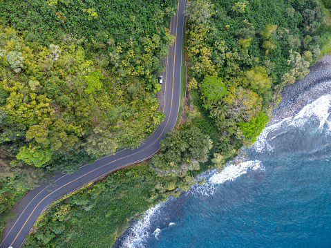An aerial view of a winding road along a lush tropical coastline with crystal clear turquoise water. Road to Hana, Maui Hawaii.