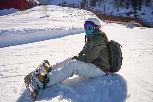 Snowboarder seated in the snow, taking a moment to rest on a sunny slope.