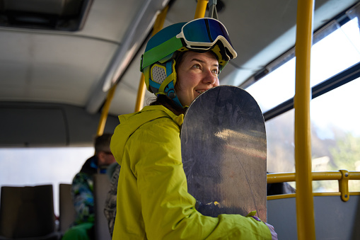 Cheerful snowboarder holding a snowboard on a bus to the ski slopes.