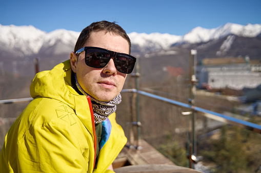 Skier in a bright jacket and sunglasses with a serene mountain landscape behind him.