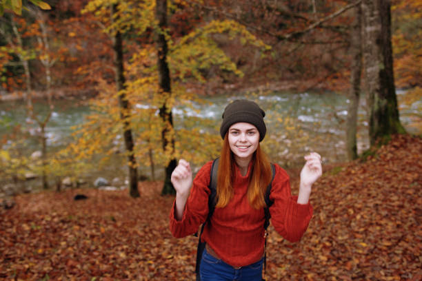 joyful woman in a hat sweater with a backpack on her back gestures with her hands in a park in nature. High quality photo