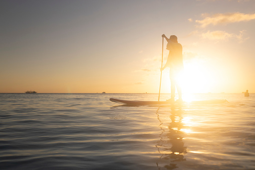 A woman enjoys stand-up paddle boarding during a magnificent sunset