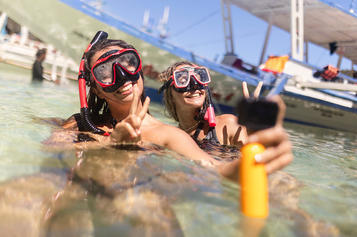 Two female friends with diving goggles filming themselves with a wearable camera