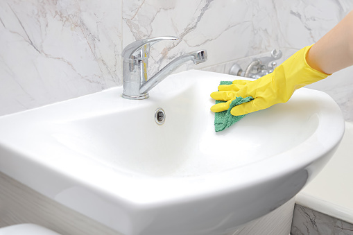girl in rubber gloves washes the white sink in the bathroom. Spring general or regular cleaning.