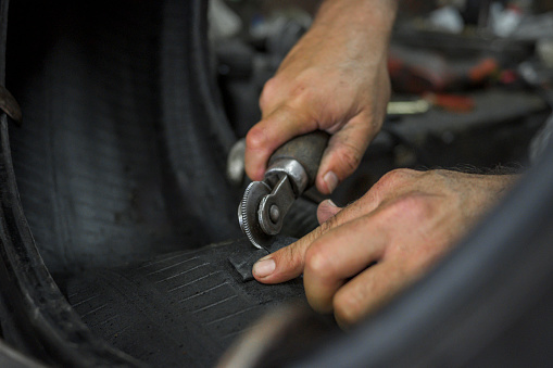 close up hands of man carving a tire with a hand tool to vulcanize the tire and patch it