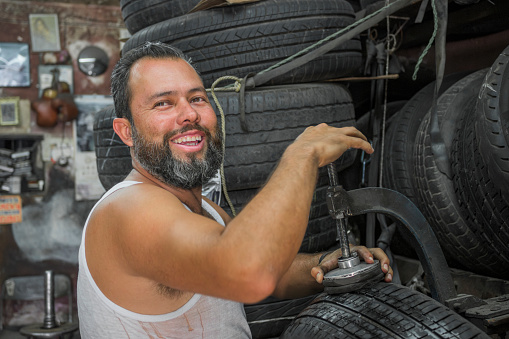portrait of smiling young adult man looking at camera while fixing a tire in his garage