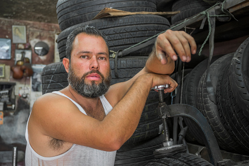portrait of young adult man looking at camera while fixing a tire in his garage