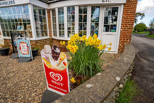 Thurne, Norfolk, UK  March 16 2023. A Walls ice cream sign, and daffodils, outside a small and local village shop