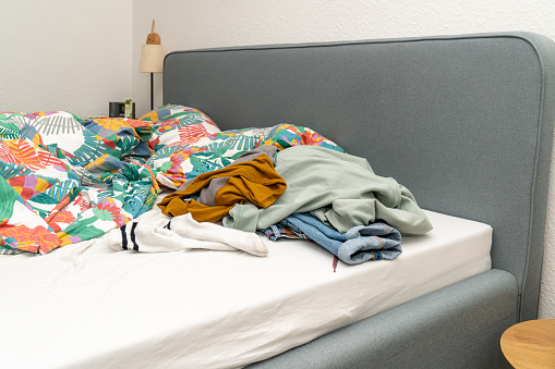 A pile of clothes on the bed in the room. A mess, clothes scattered on the bed. Fast fashion concept.