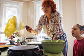 Red-haired woman deftly flips a pancake on electric skillet, teaching her daughter to cook early in the morning