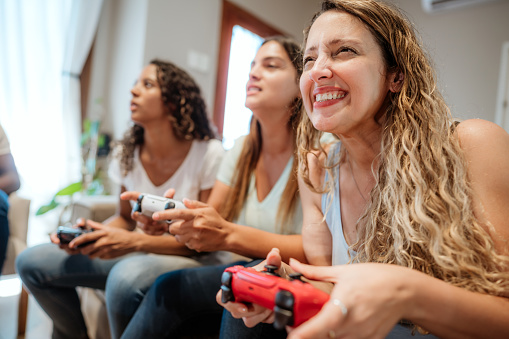Three enthusiastic female friends playing video games together and experiencing intense gameplay in a cozy living room.
