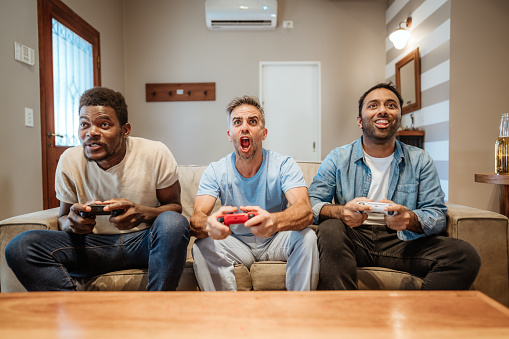 Group of friends having fun playing video games together on couch, bonding over a shared hobby and laughter.