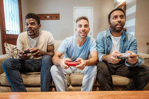 Three male friends enjoying their time playing video games together, sitting on the couch with game controllers in hand.